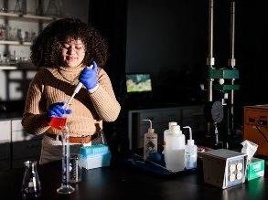 高中学生玛蒂·史密斯在化学实验室里，她面前的桌子上放着一个灯泡注射器和一个烧杯，还有其他化学设备